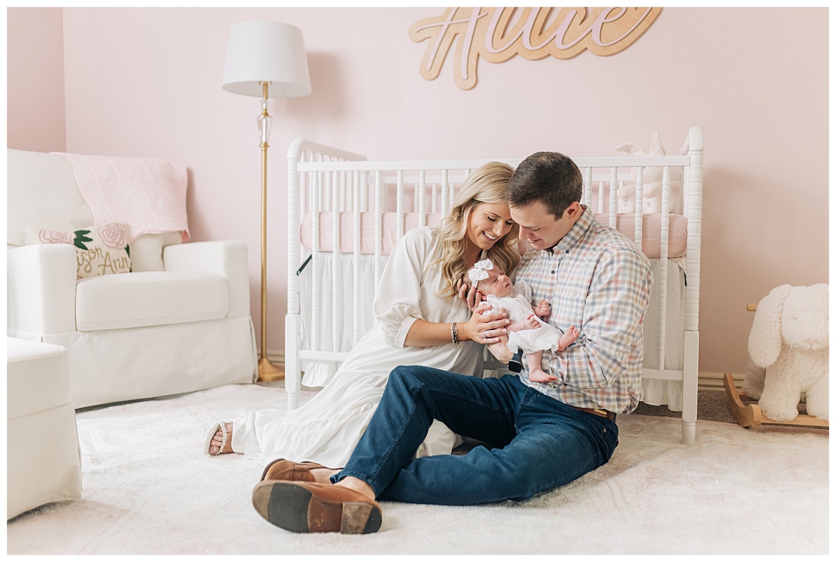 Photo of mom, dad and newborn baby in the nursery sitting in front of crib taken by Fayetteville photographer grace Starr photography 