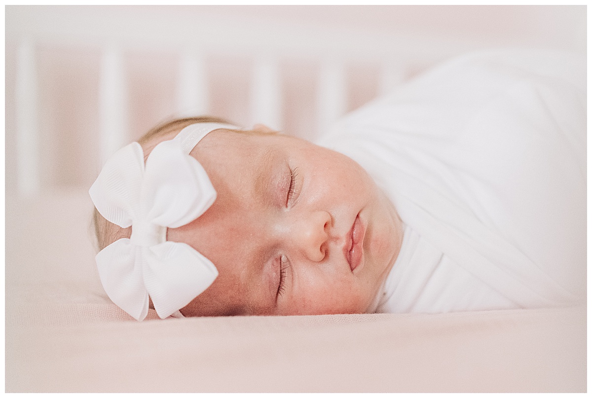 photo of newborn baby with white bow laying in bed taken by northwest Arkansas photographer grace Starr